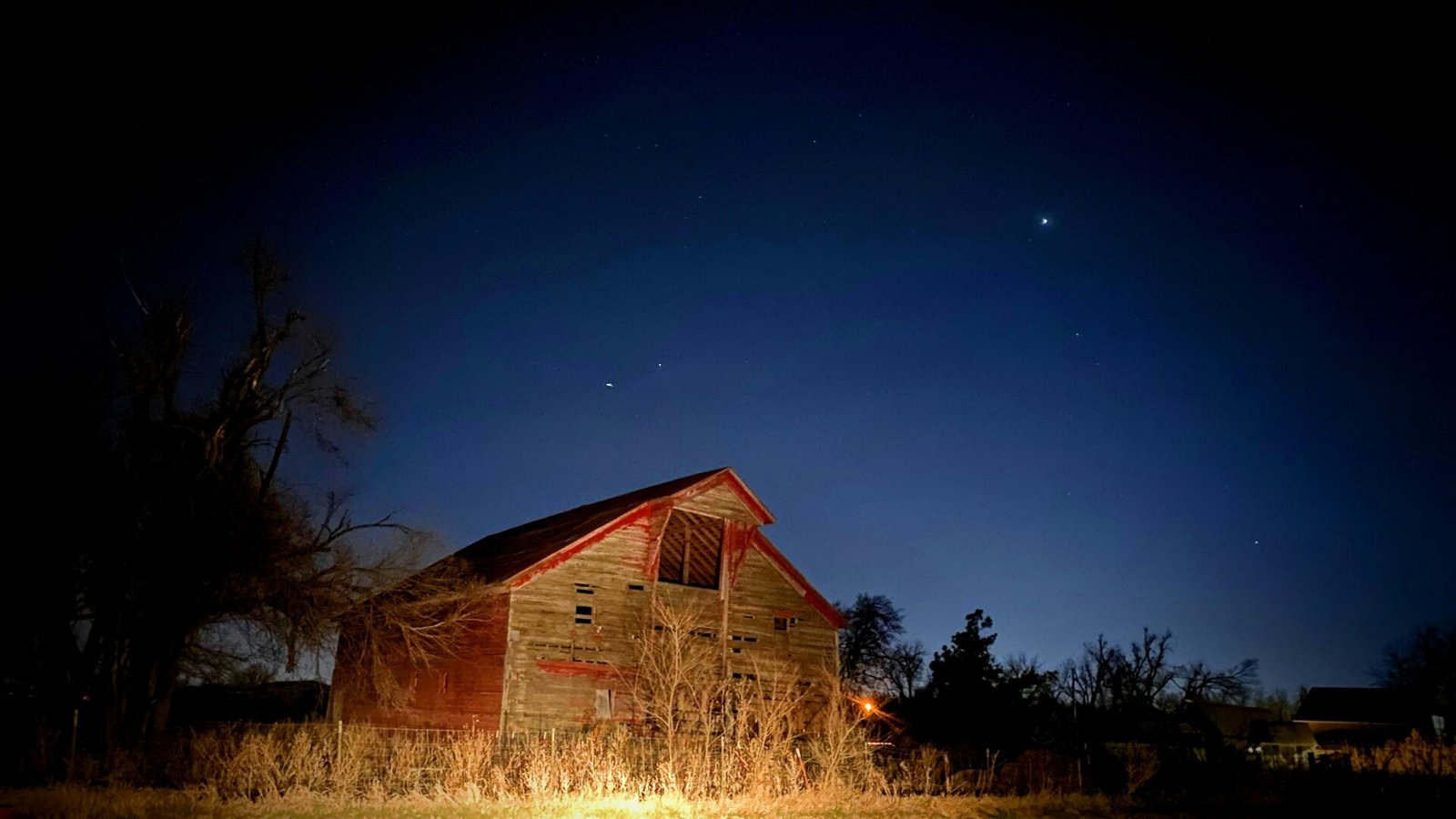 a barn lit up at night with the moon in the sky