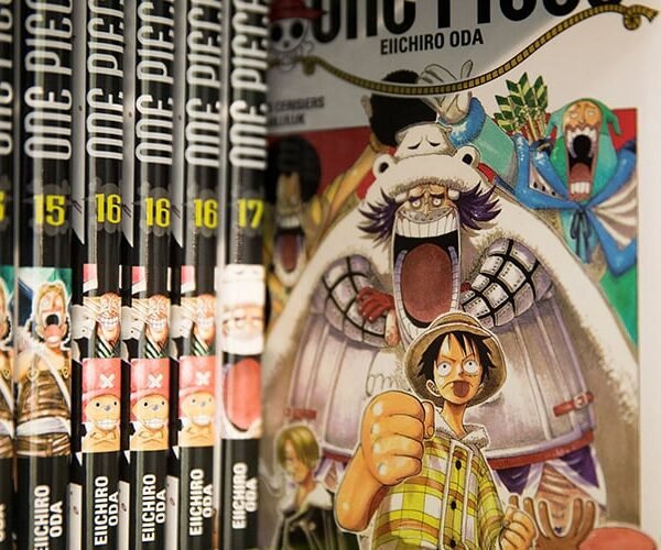 An open laptop displaying One Piece manga online, surrounded by books and coffee in a cozy reading setting.